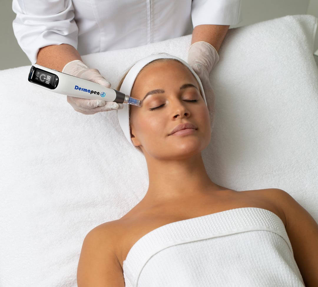 A woman lying on a bed at a beauty clinic receiving microneedling treatment on her face.